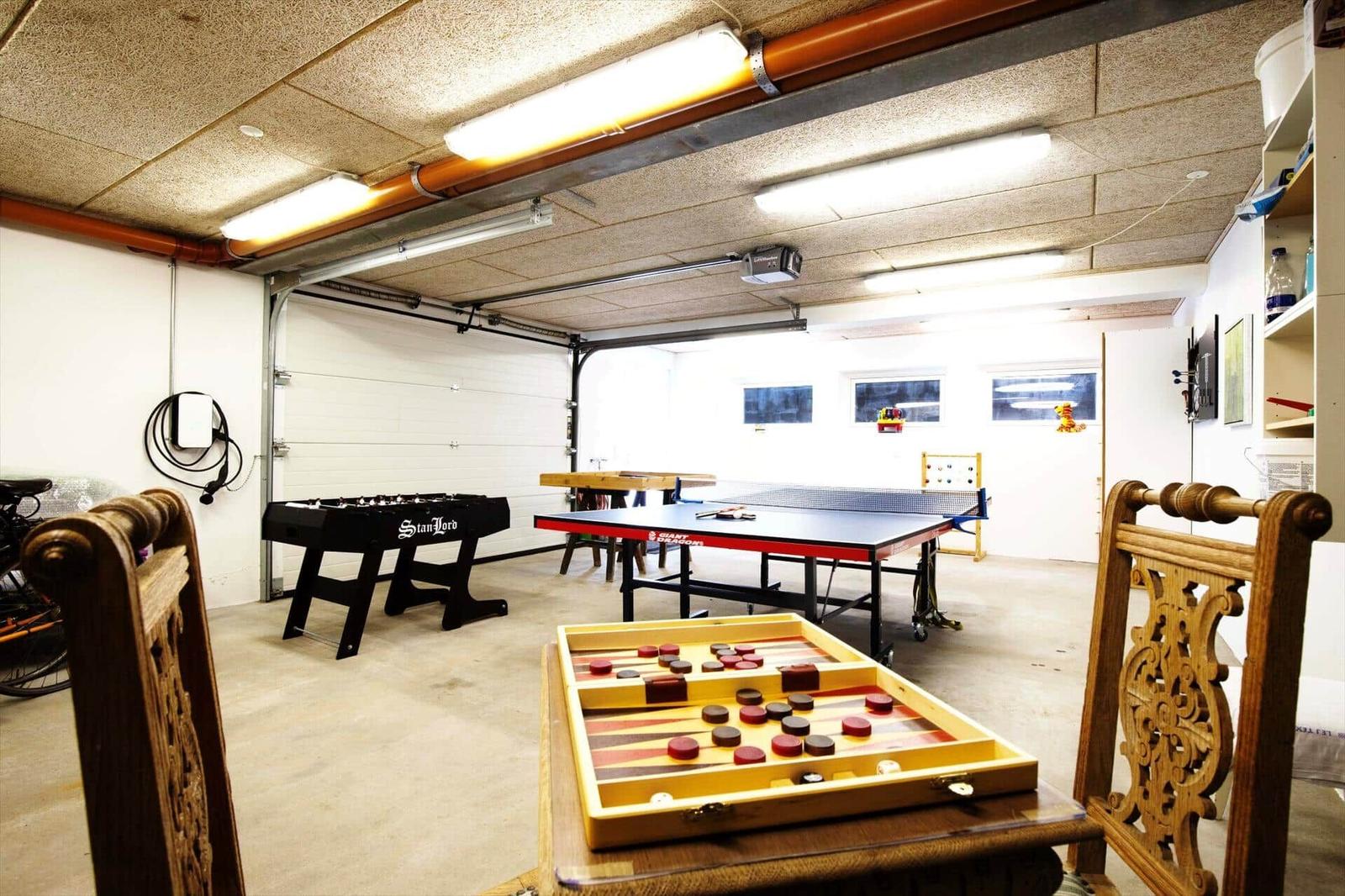 Garagenraum mit Tischtennisplatte, Backgammon und Fussballtisch. Holzstühle und Deckenleuchten sichtbar.