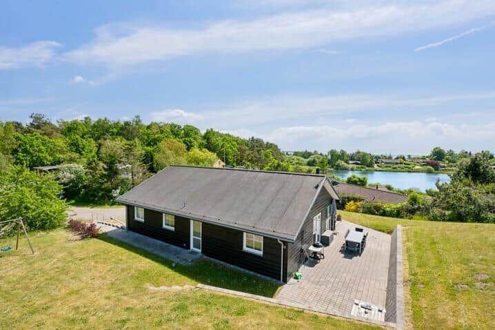 Schwarzes Haus mit Terrasse und Blick auf See und Wälder.