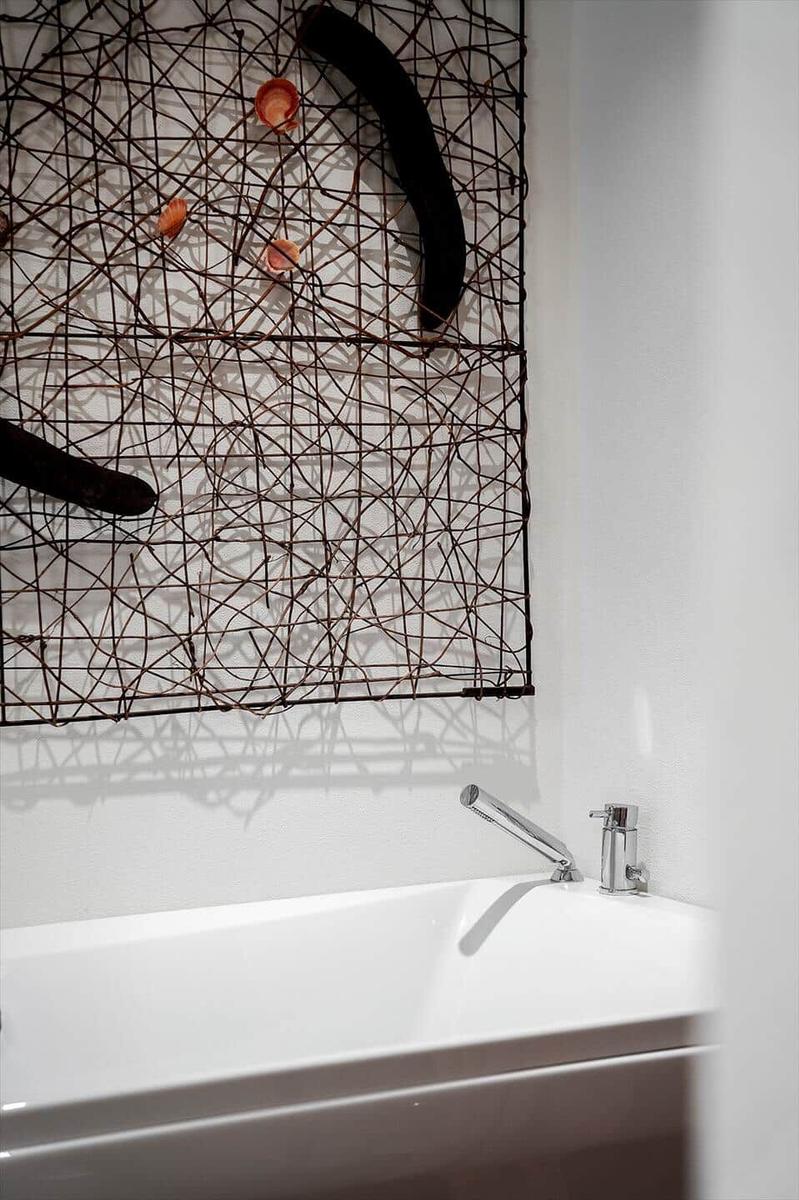 Bad mit weißen Wänden, Badewanne und Wanddekoration aus Draht.