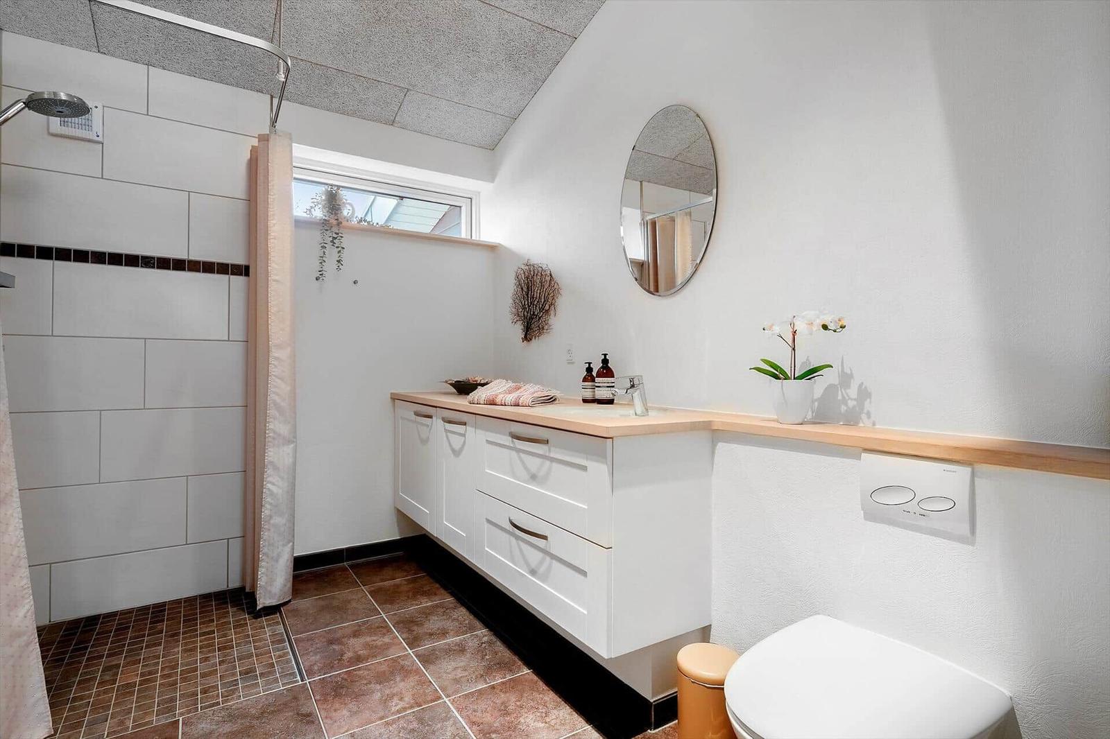Badezimmer mit Dusche, Waschbecken und Toilette. Holzoberfläche und Spiegel.