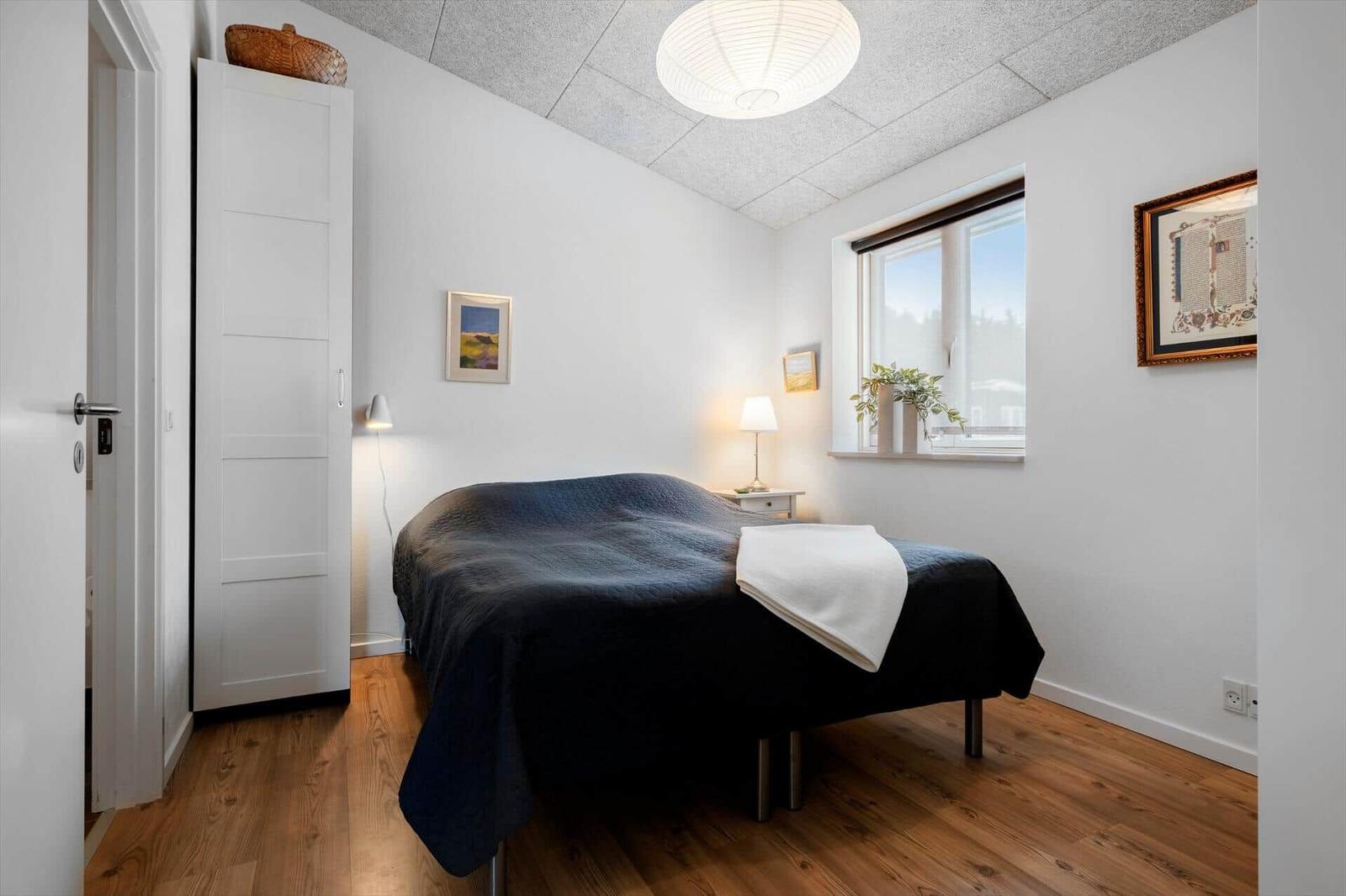 Schlafzimmer mit Bett, Kleiderschrank und Fenster.