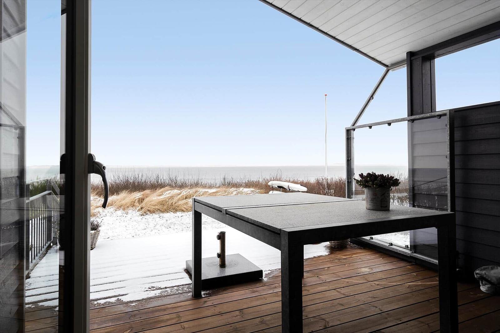 Terrasse mit Tisch und Blick aufs Meer und Dünen.