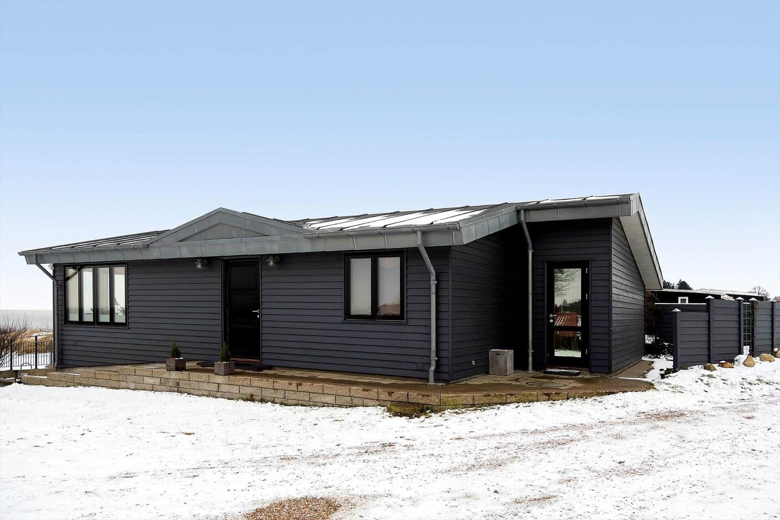 Moderne, schwarz getäfelte Ferienhaus mit Dachgauben und schneebedecktem Grundstück.