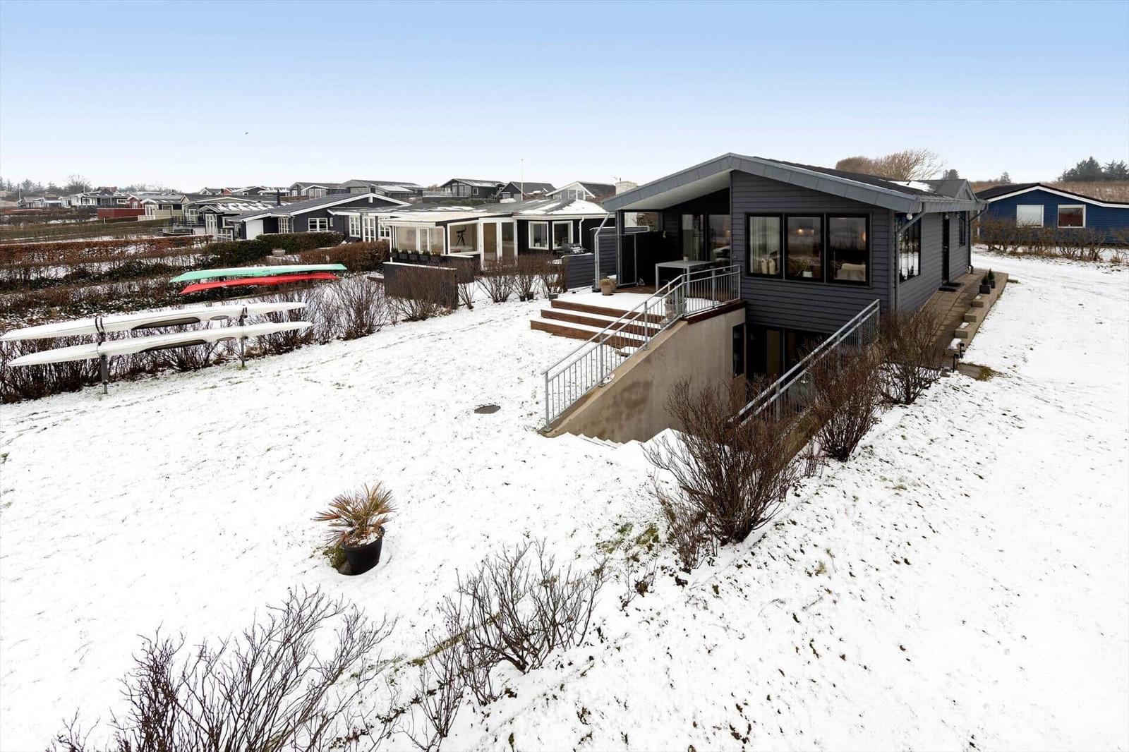 Moderne Villa mit Terrasse und Schneeflächen. Mehrere Kanus stehen im Garten.