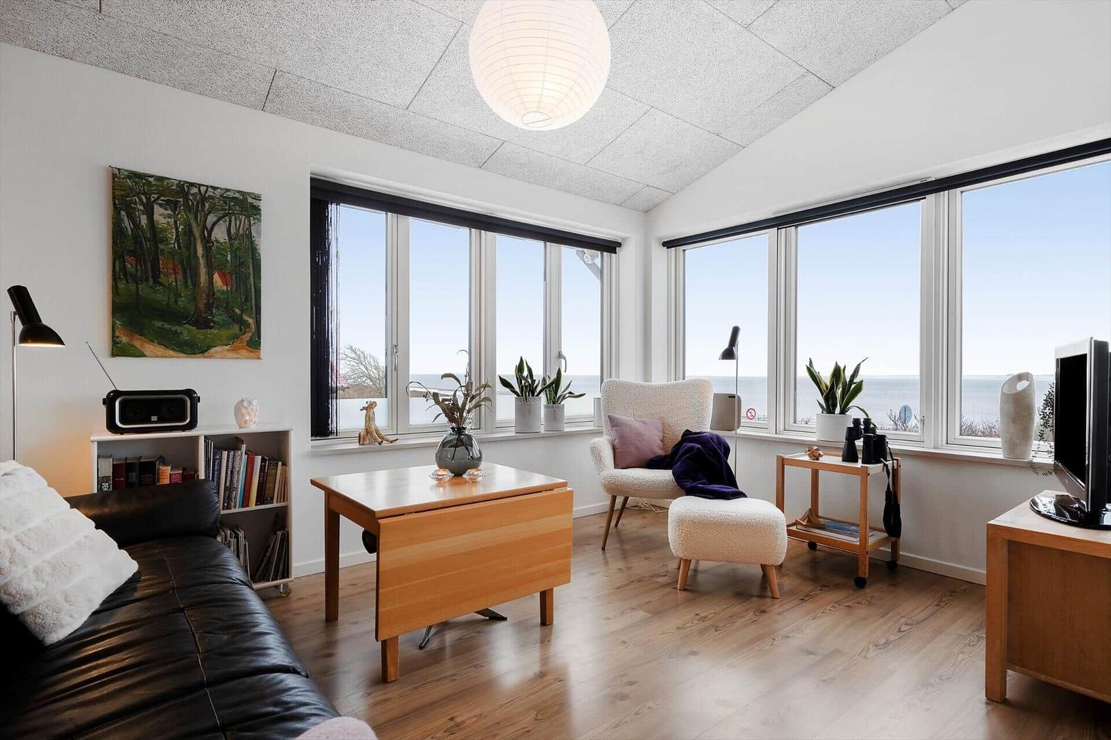 Wohnzimmer mit großem Fensterblick aufs Meer, Sofa, Sessel und Holzmöbel.