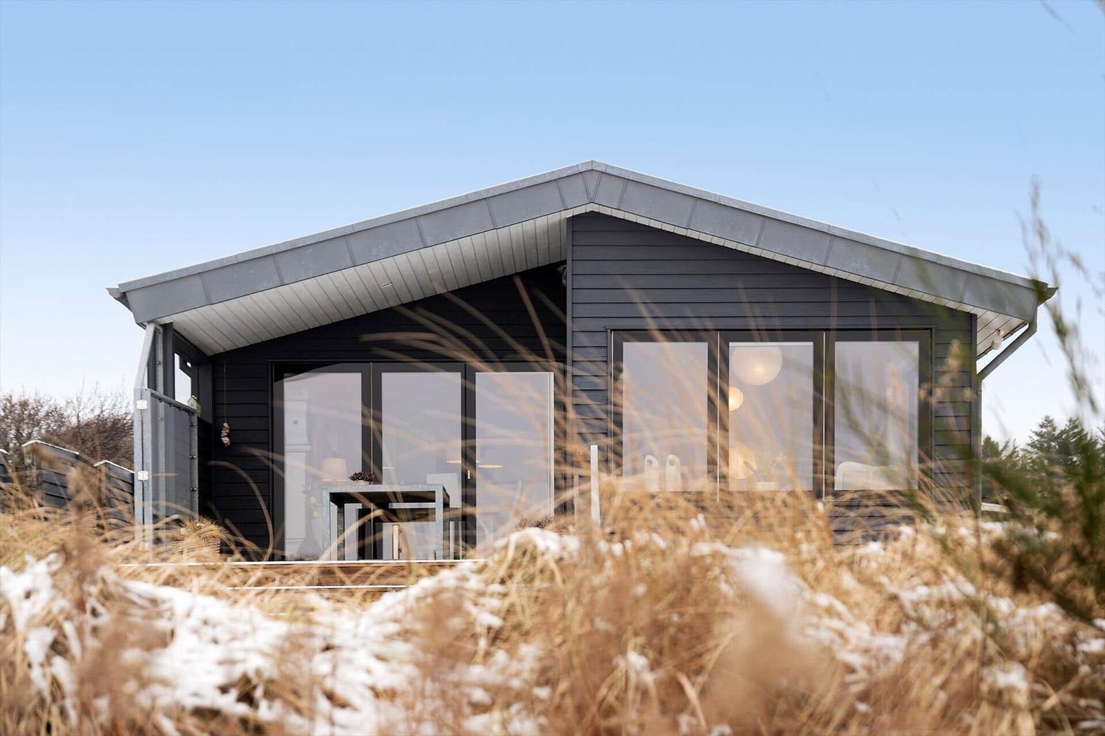 Moderne Villa mit großem Fensterbereich und schneebedecktem Gras im Vordergrund.