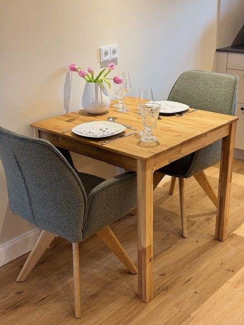 Holztisch mit zwei Stühlen, Tischdecke, Gläser und Blumen in Vase.