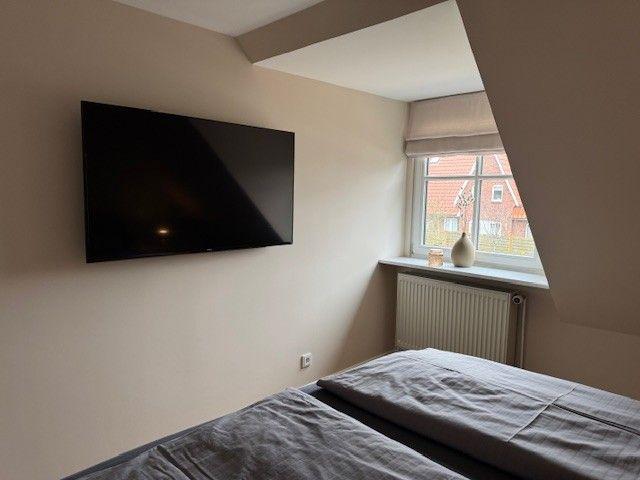 Schlafzimmer mit Bett, Wandfernseher und Fenster mit Blick nach draußen.