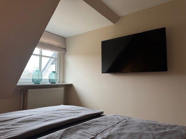 Schlafzimmer mit Dachschrägen, Fenster und Wandfernseher.