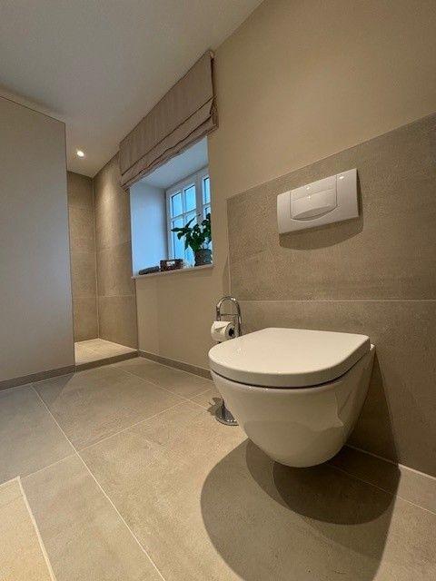 Badezimmer mit Toilette, Fenster und Fliesenboden.