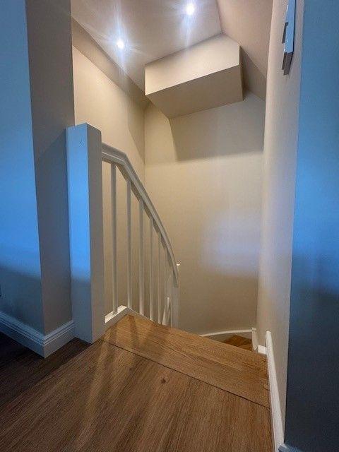 Treppenhaus mit Holzstufen und weißer Brüstung. Deckenleuchte und neutrale Wände.