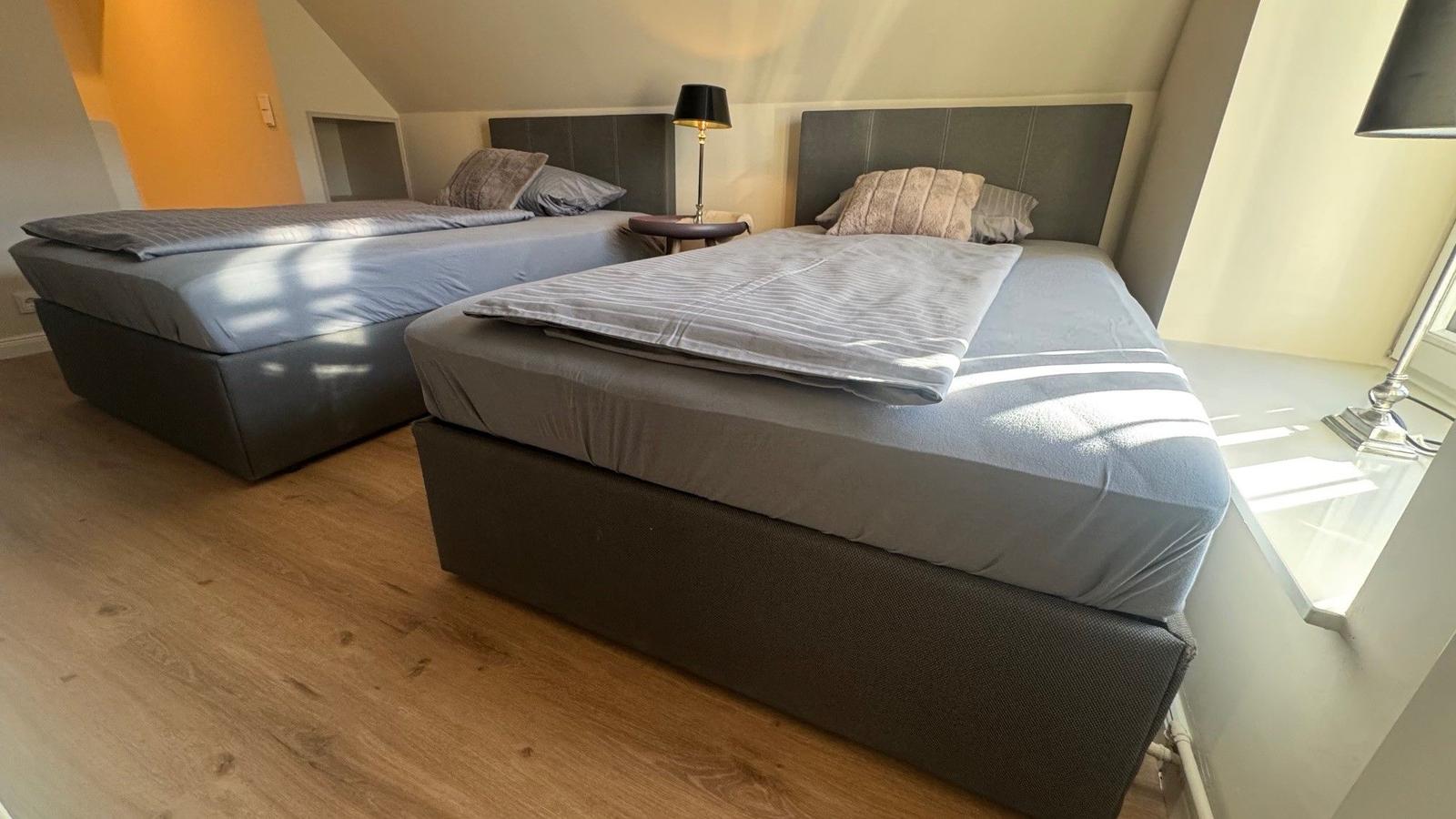 Zwei Betten mit grauer Bettwäsche und Kopfteil in einem Schlafzimmer mit Holzboden und Dachschrägen.