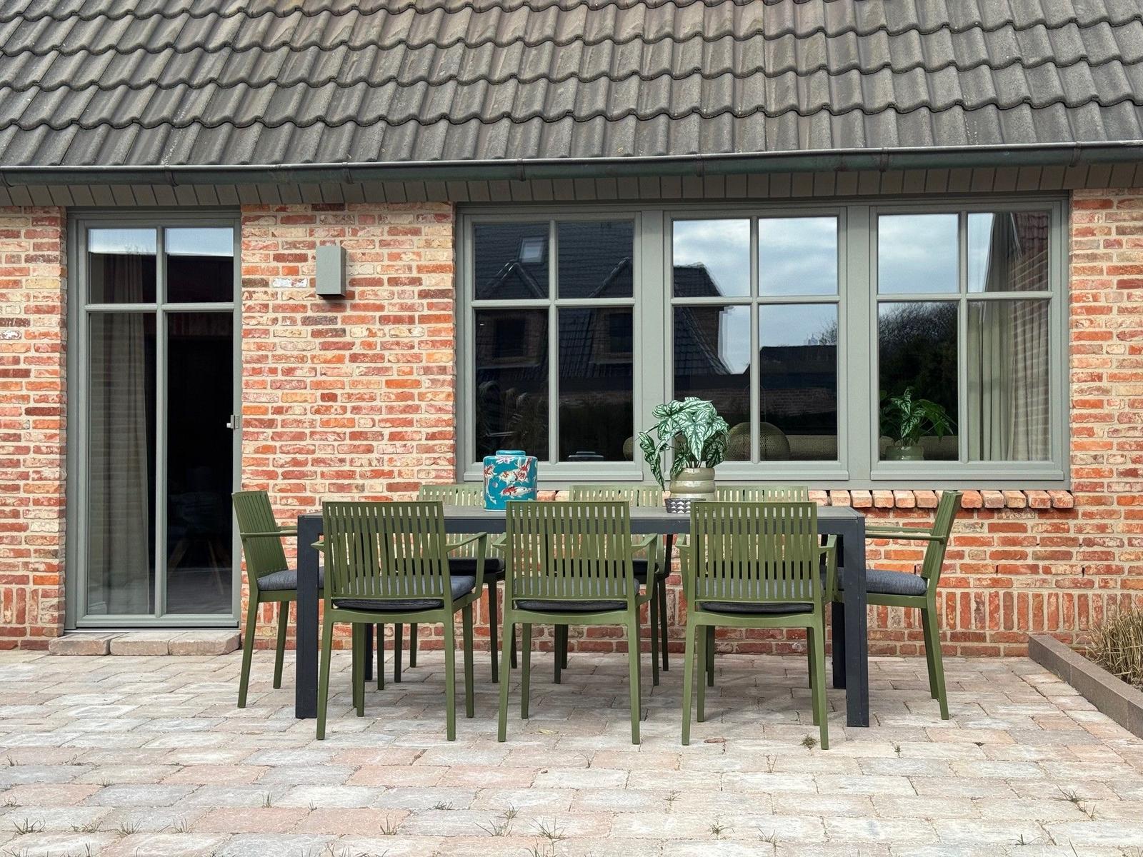 Außenbereich mit Tisch und Stühlen vor einem Backsteinhaus mit Fenstern.