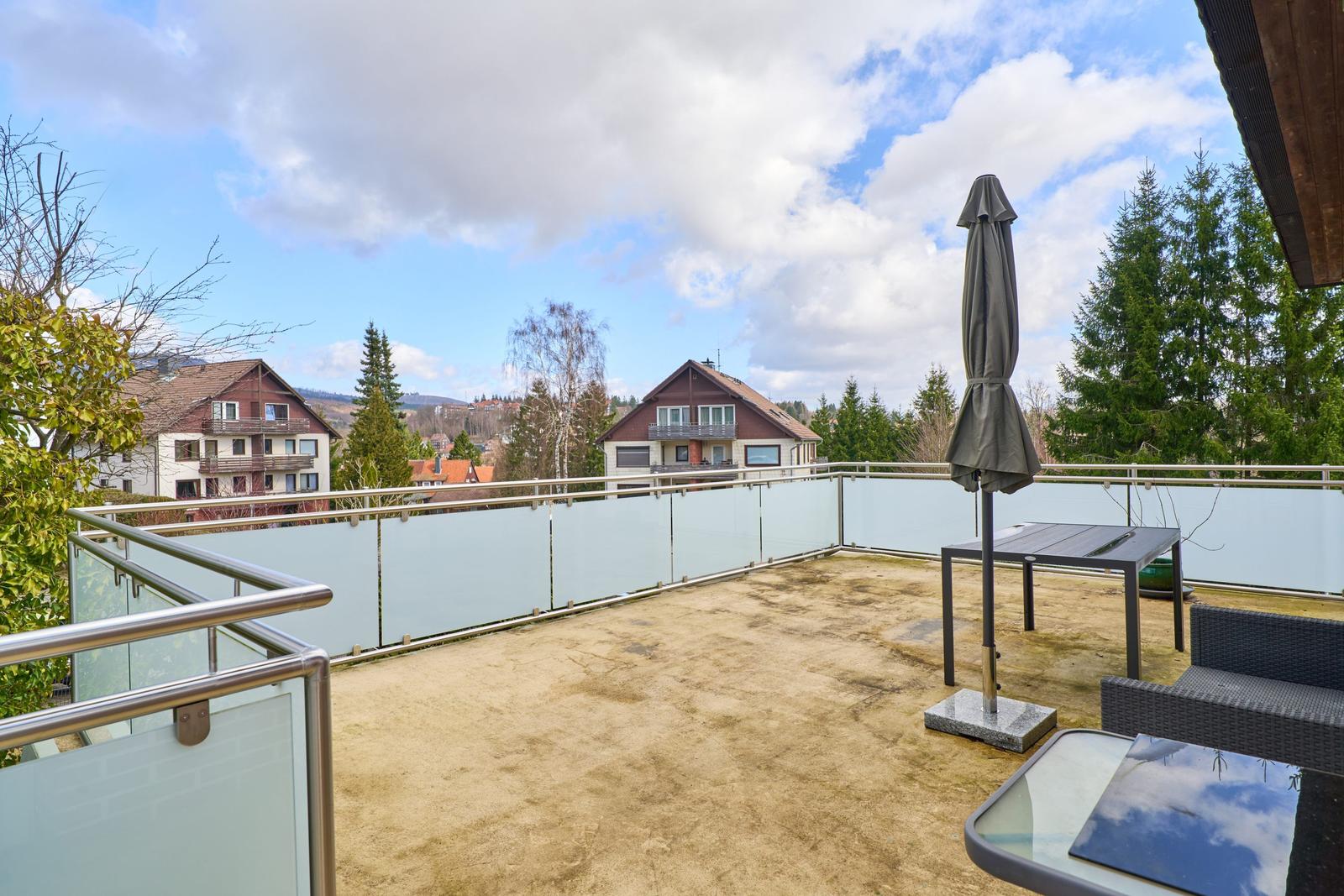 Terrasse mit Tisch, Stühlen und Sonnenschirm. Blick auf Häuser und Bäume.