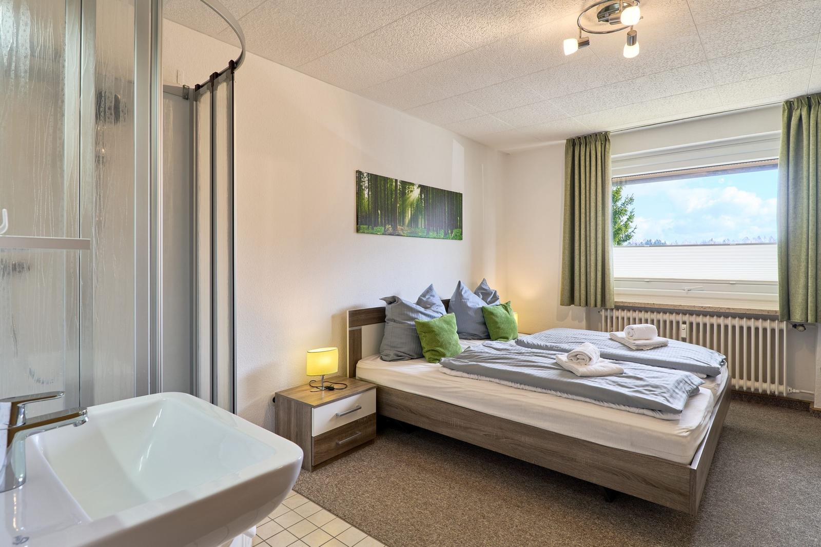 Schlafzimmer mit Doppelbett, Fenster und integriertem Bad.