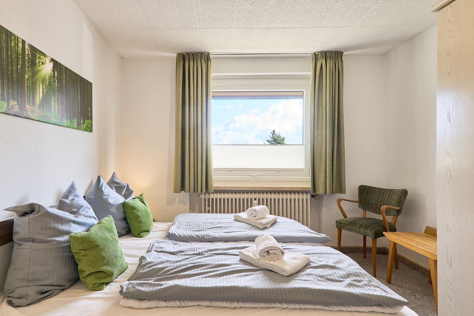 Zimmer mit Doppelbett, Fenster, Stuhl und Wandbild