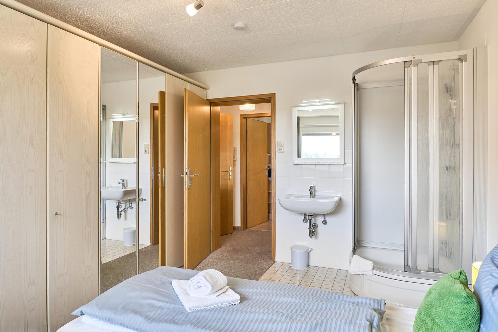 Schlafzimmer mit Dusche, Waschbecken und Kleiderschrank. Durchgang zu weiteren Räumen.
