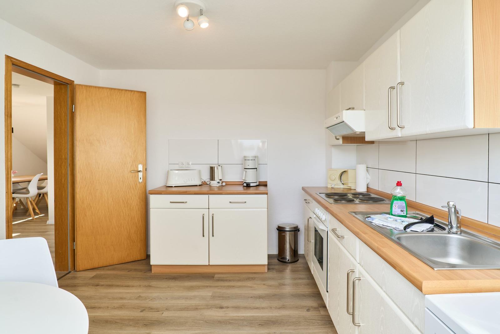 Küche mit Arbeitsplatte, Spüle und Kochfeld. Tür führt in Wohnbereich.