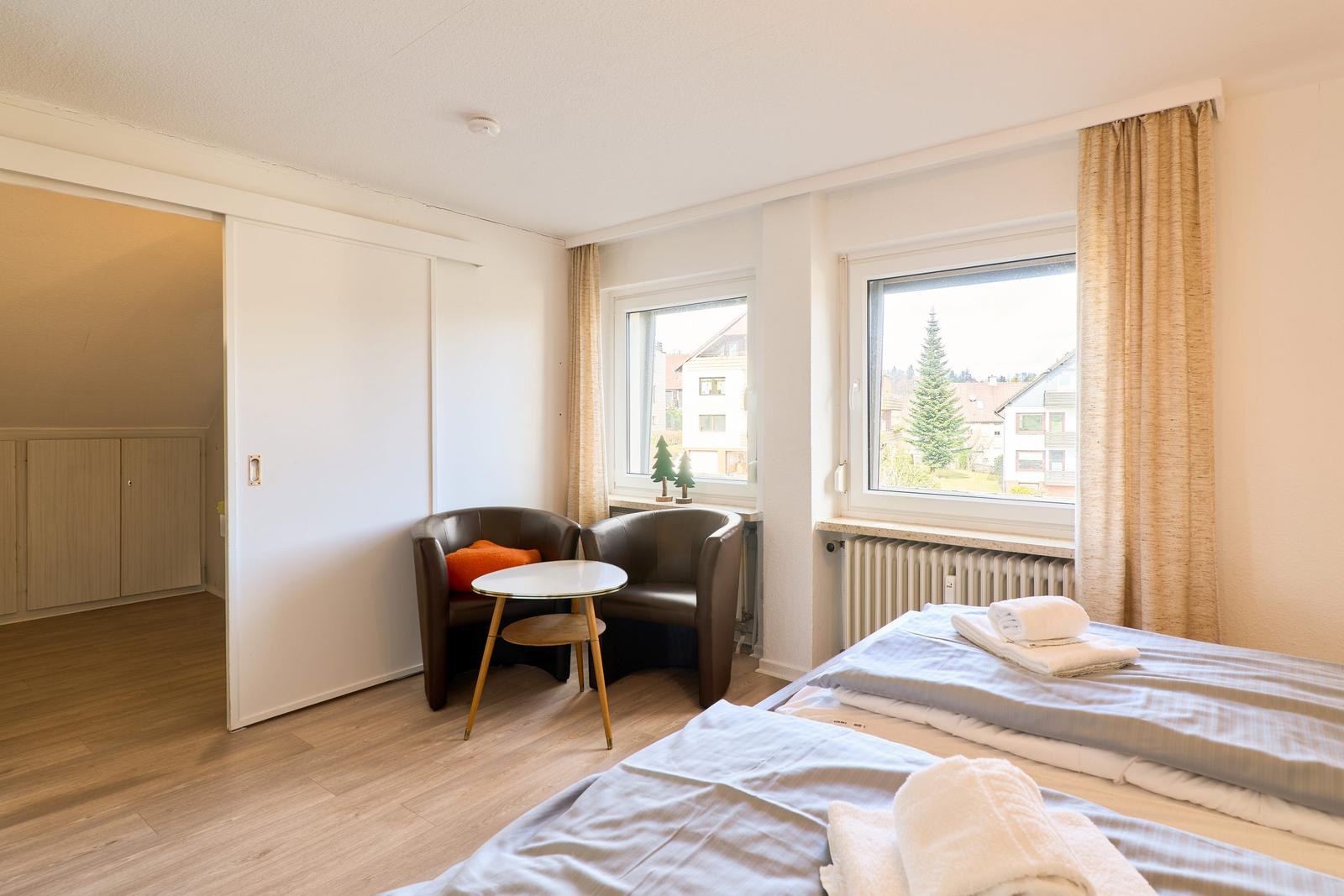 Zwei Betten, zwei Fenster, zwei Sessel und ein kleiner Tisch.