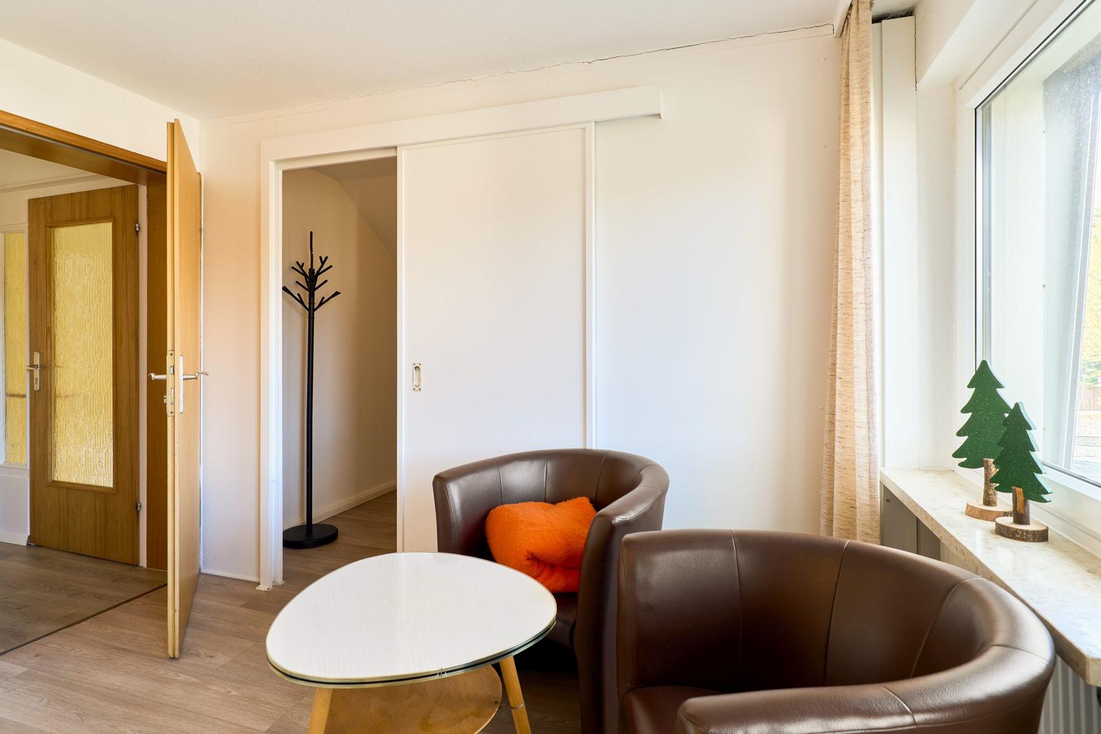 Zwei braune Sessel und ein runder Tisch stehen vor einem Fenster mit grünen Dekorationen.