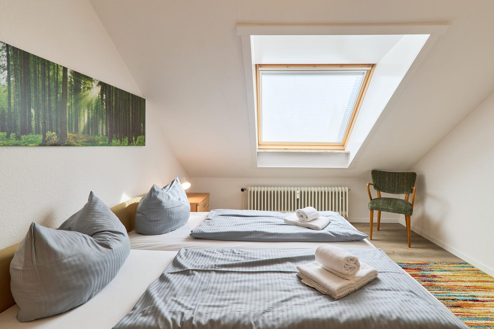 Zimmer mit Dachschrägen, Dachfenster, Bett und Stuhl.