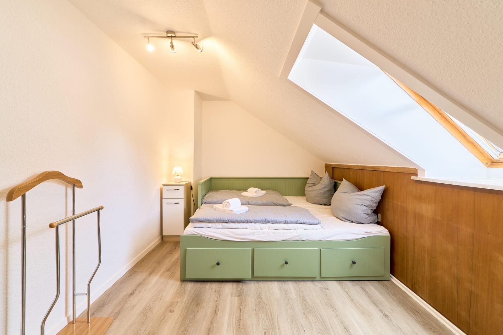 Schlafzimmer mit Dachschräge, Dachfenster und grünem Bett.