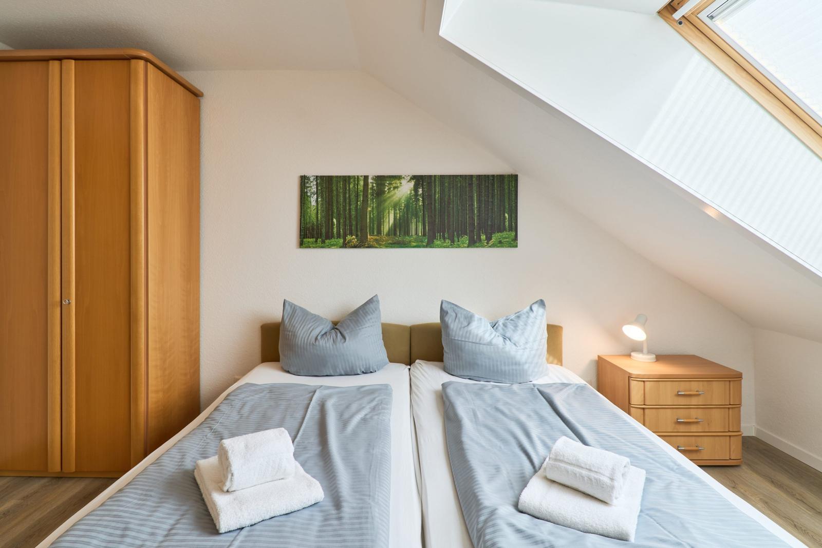 Zimmer mit zwei Betten, Schrank, Nachttisch und Dachfenster.