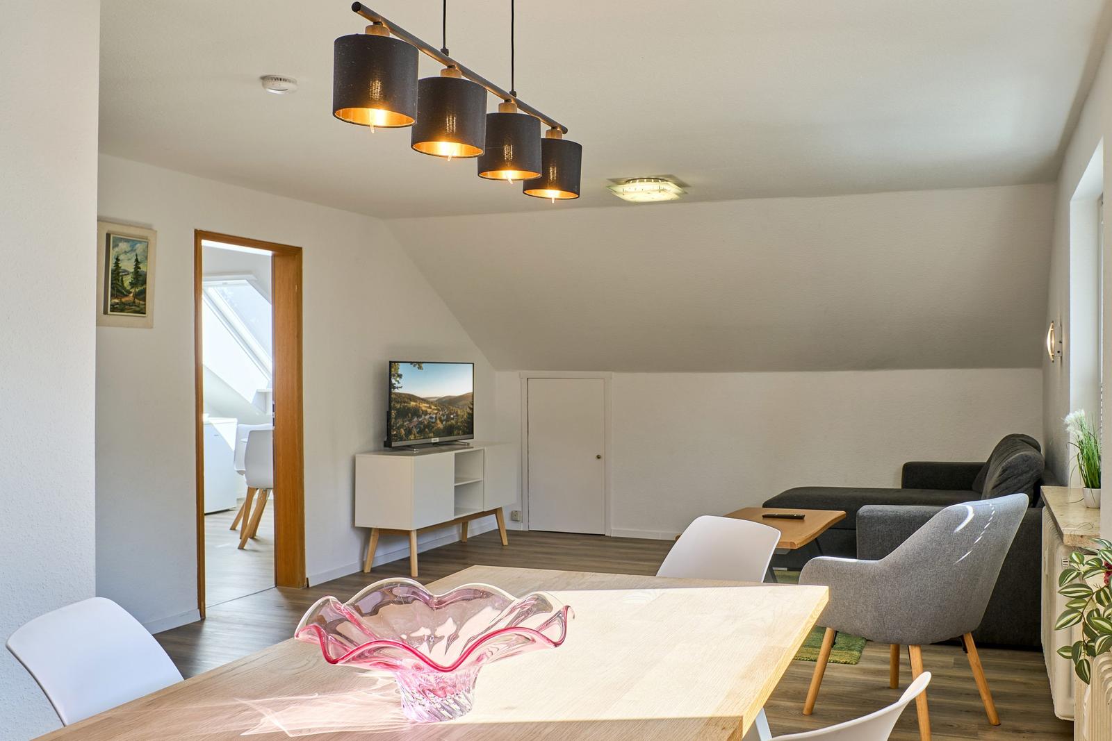 Wohn- und Essbereich mit TV, Sofa und Esstisch. Dachgeschoss mit Holzboden und Lampen.