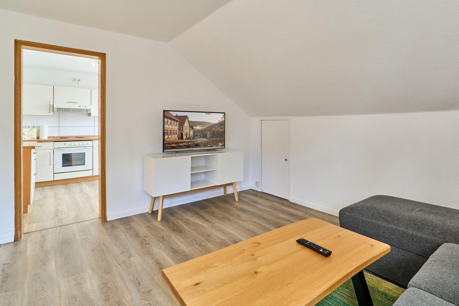 Wohnzimmer mit TV, Couch und Küche im Hintergrund.