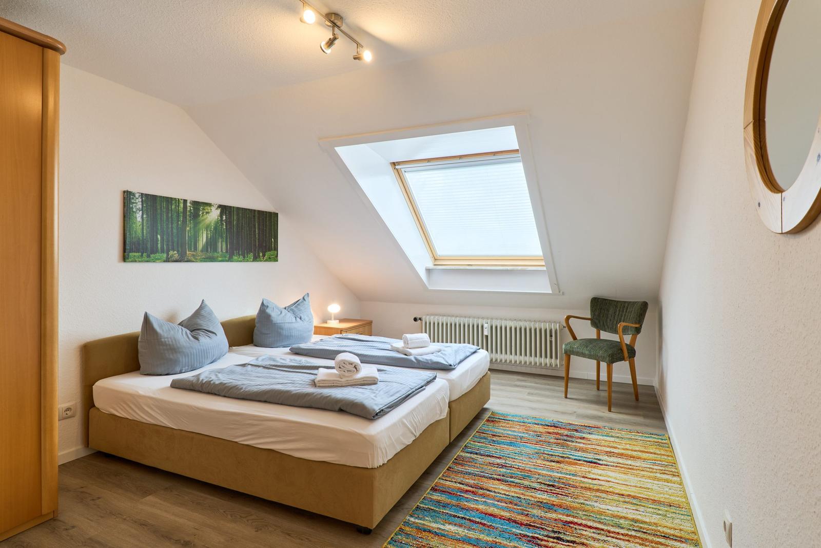 Schlafzimmer mit Dachschräge, Dachfenster, Bett, Stuhl und Teppich.