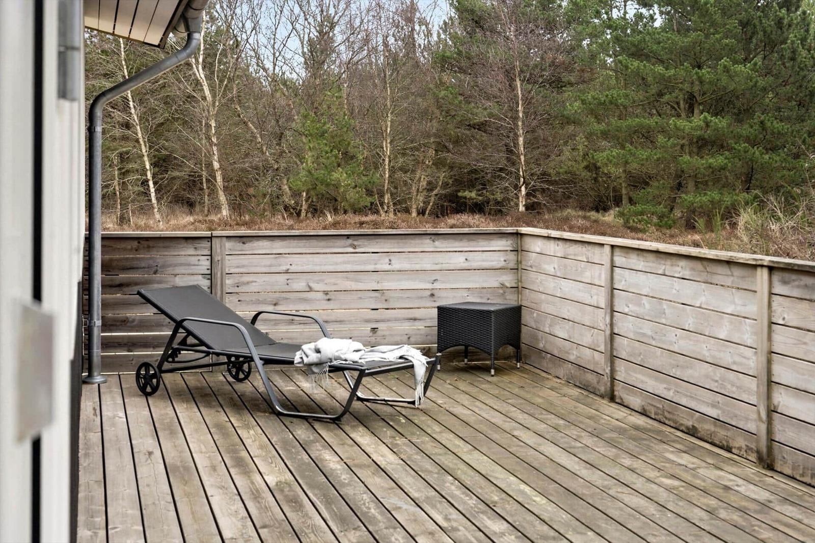 Terrasse mit Liegestuhl und Tisch, umgeben von Holzwänden und Wald.