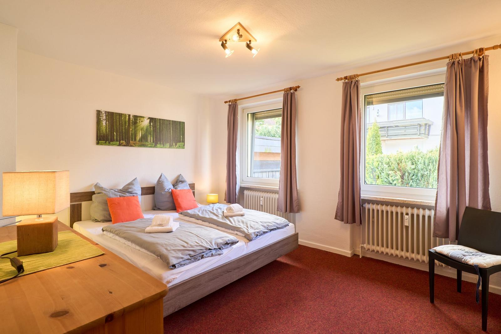 Schlafzimmer mit Doppelbett, Fenster und Holztisch.