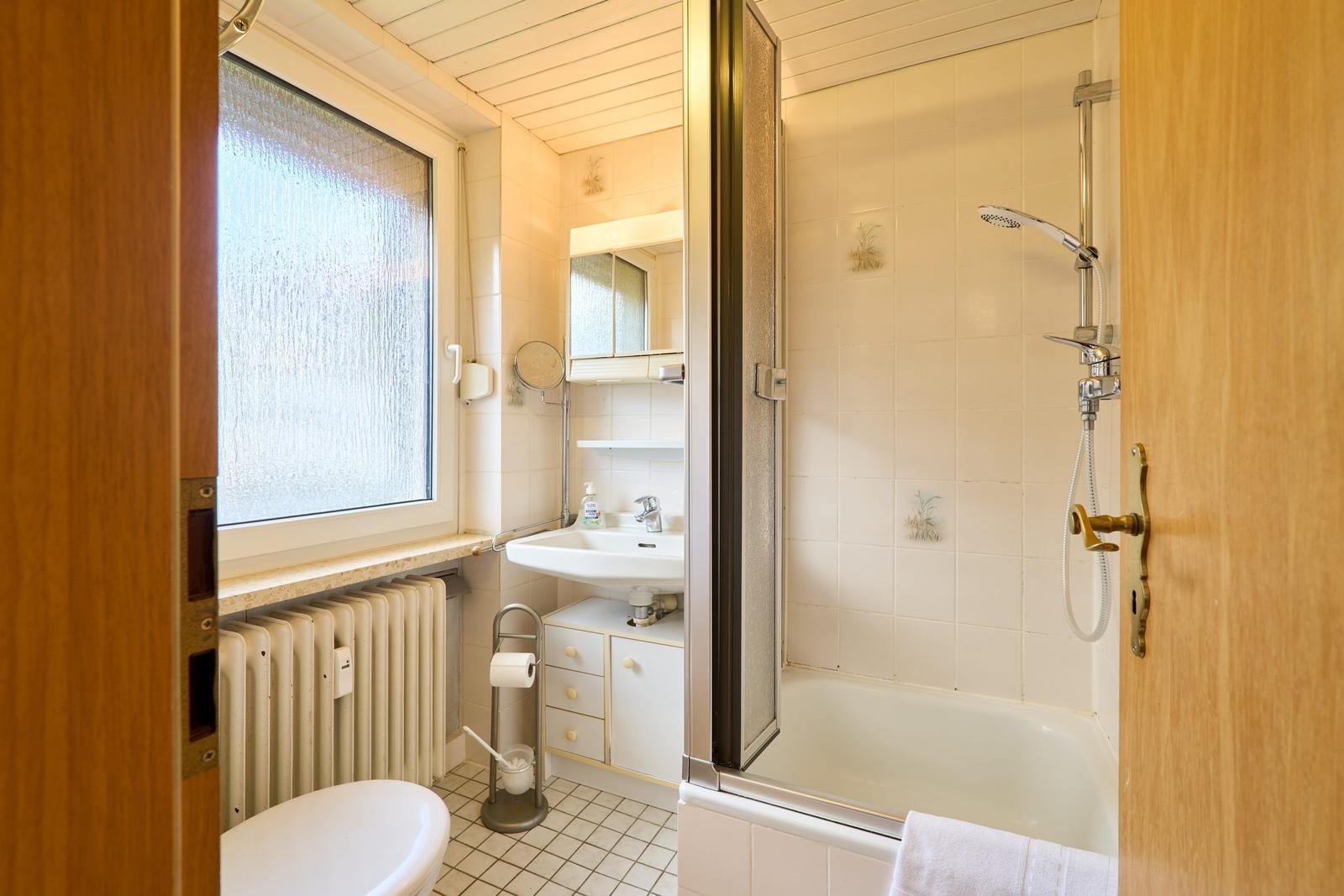 Badezimmer mit Dusche, Waschbecken und Toilette. Fenster mit getöntem Glas.