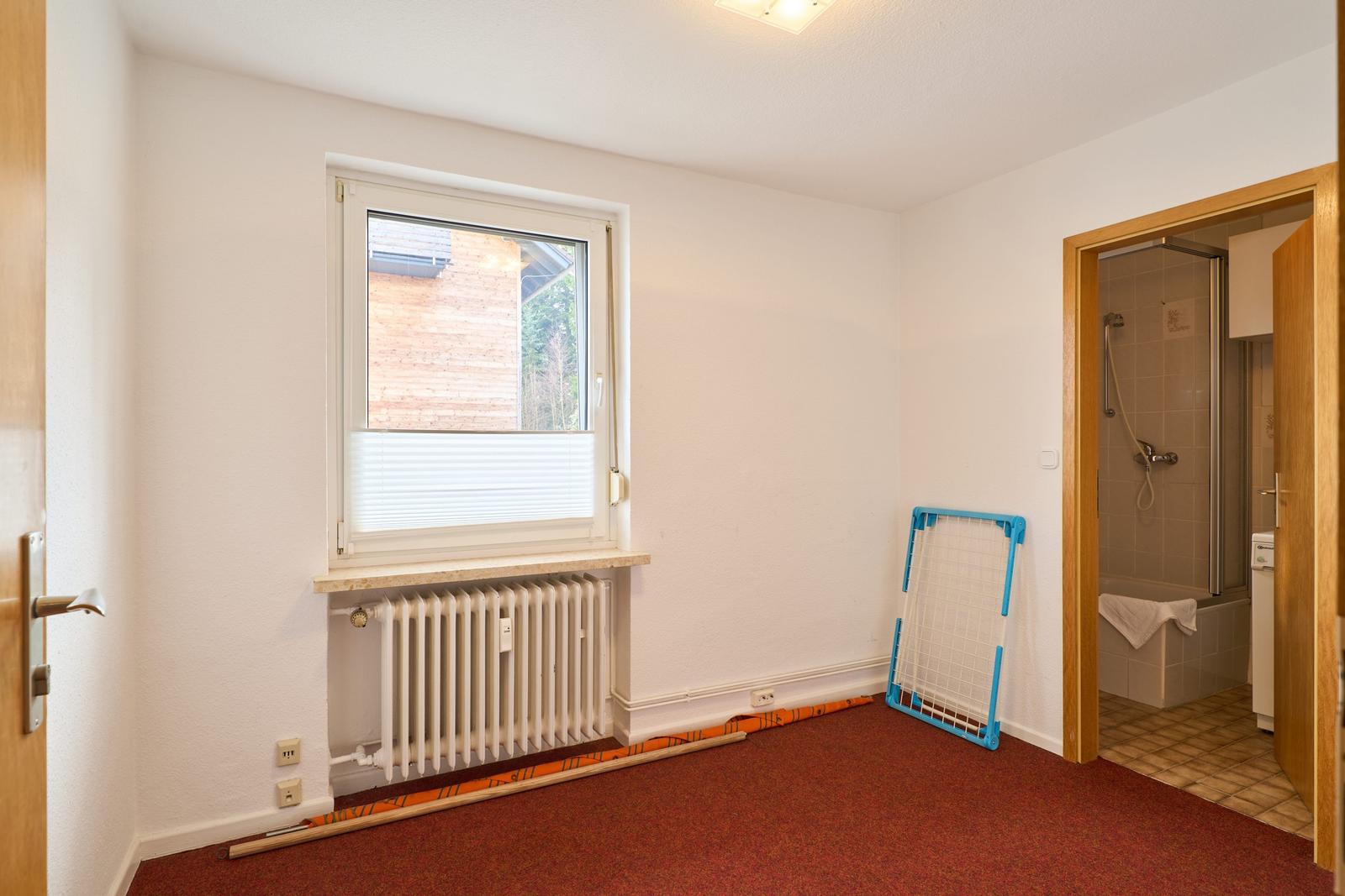 Zimmer mit Fenster, Heizkörper und Tür zum Bad.