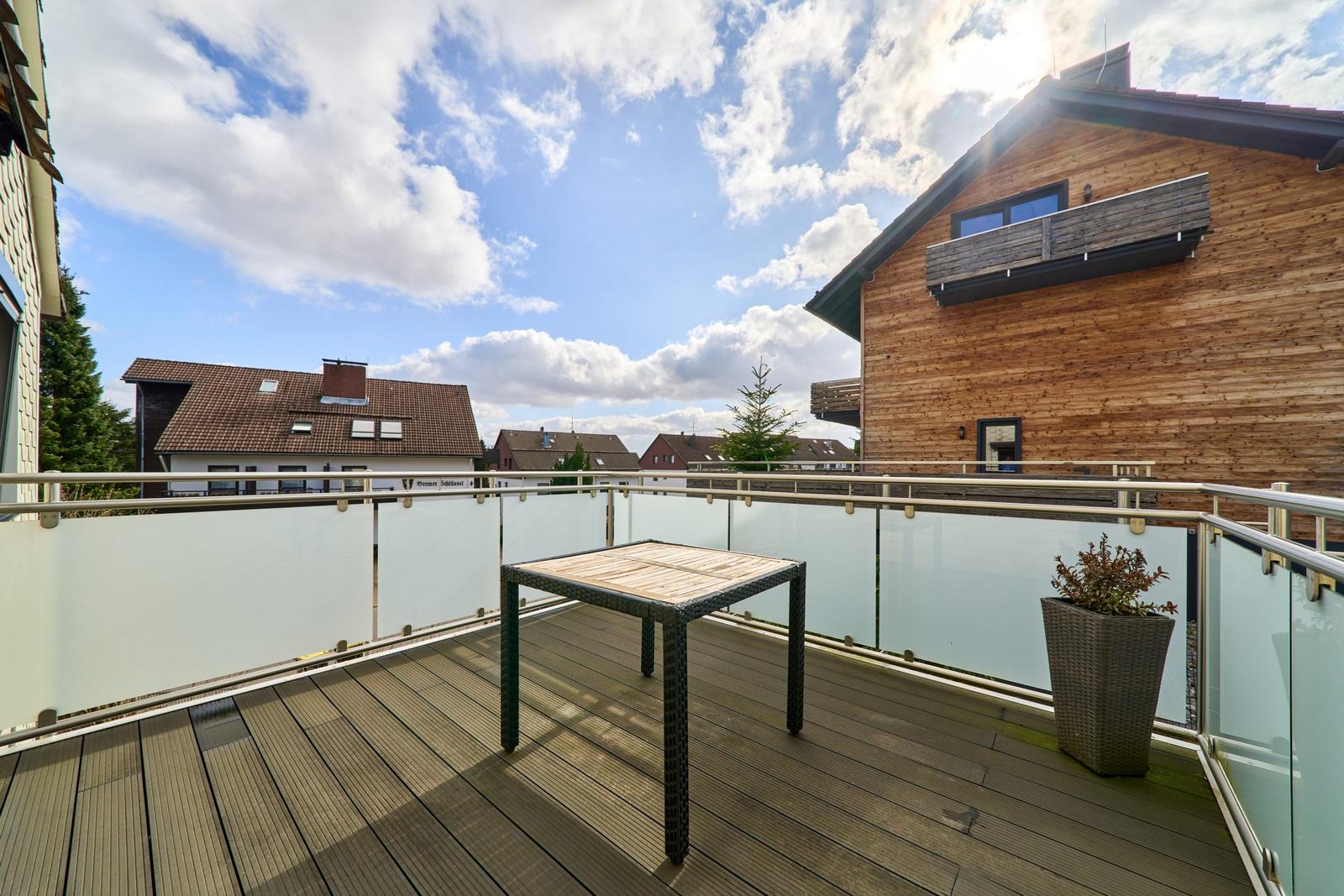 Terrasse mit Tisch und Pflanze, Blick auf Wohnhäuser und Himmel.