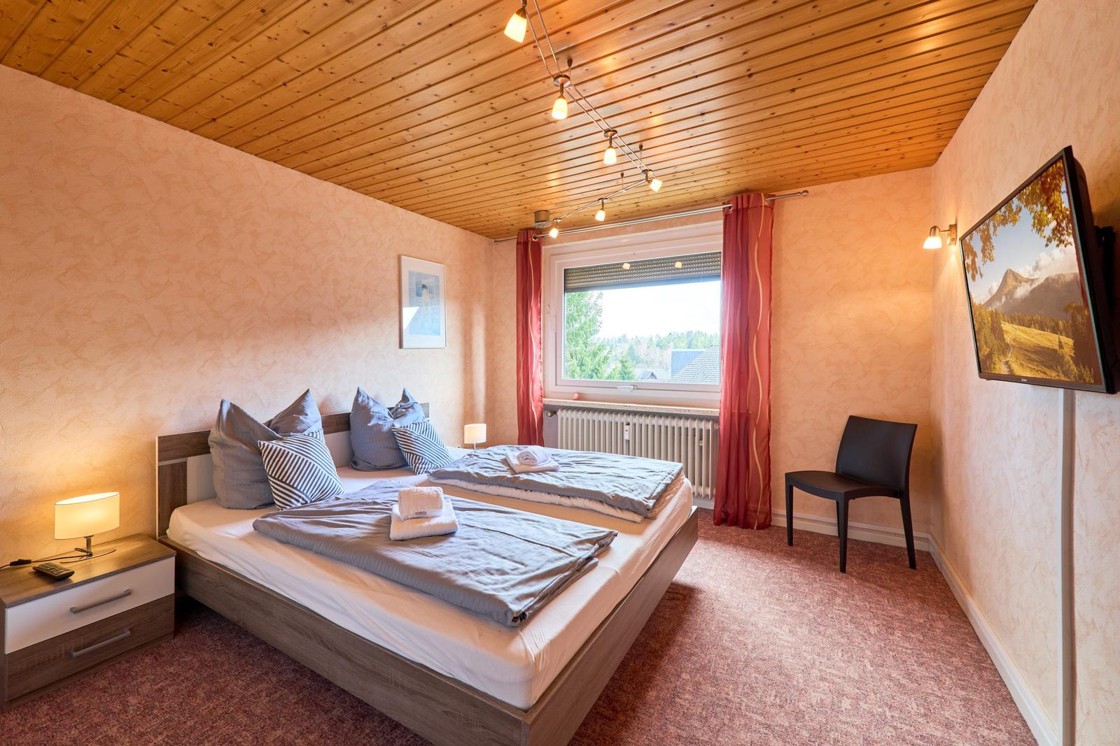 Schlafzimmer mit Doppelbett, Fenster, TV und Nachttisch.