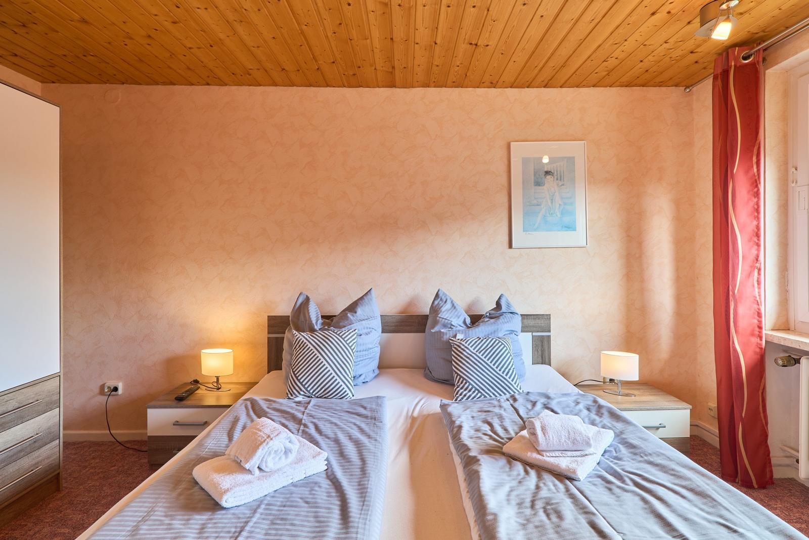 Zimmer mit Doppelbett, Nachttischen und Holzdecke.