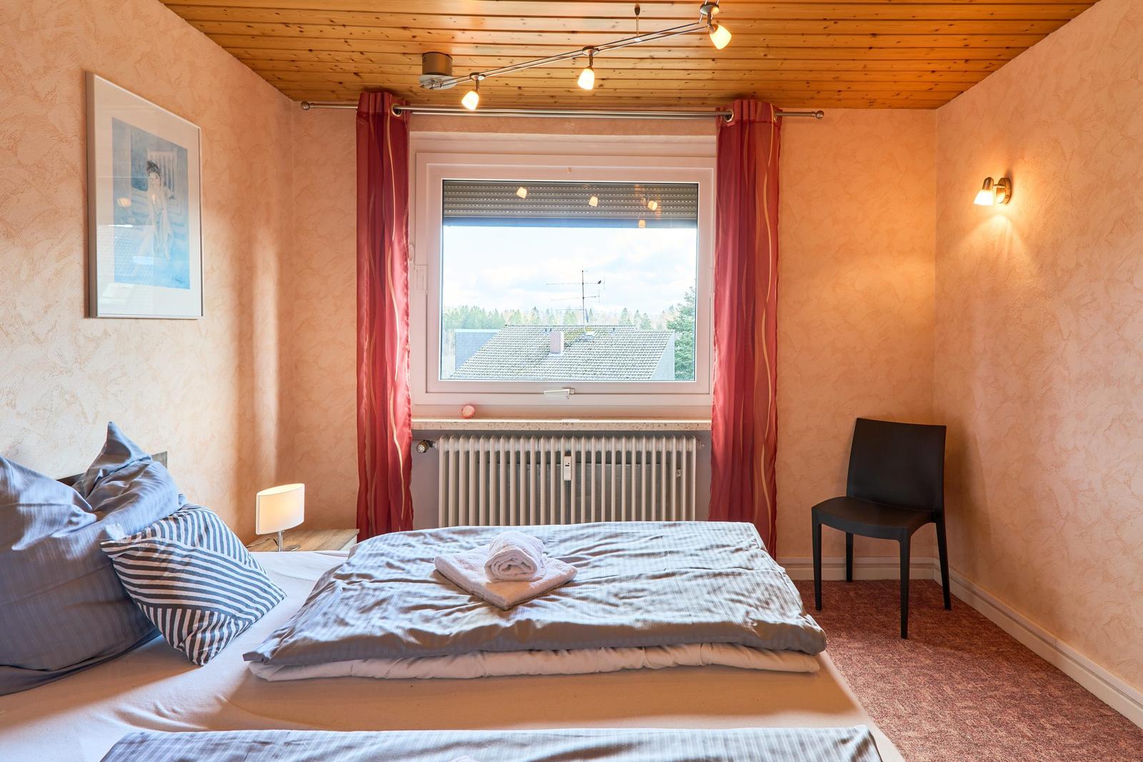 Schlafzimmer mit Bett, Fenster, Stuhl und Decke.