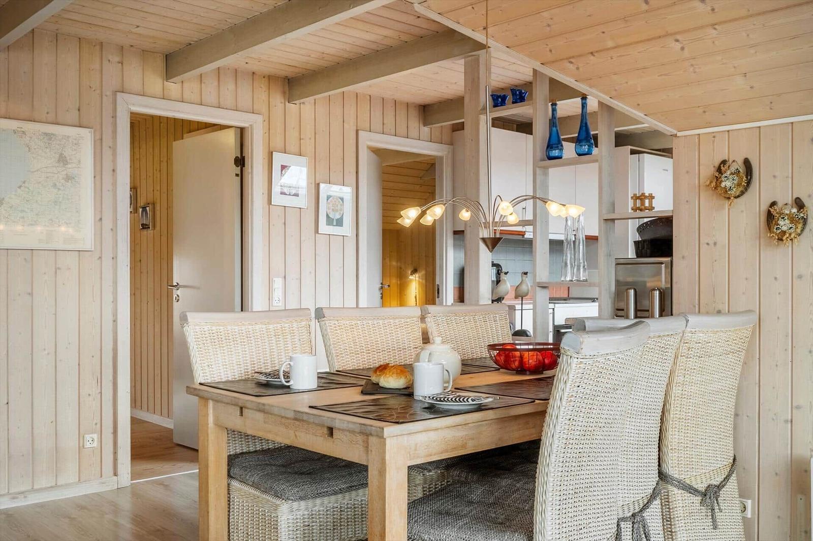 Esszimmer mit Holzwand und Esstisch mit Stühlen. Küche im Hintergrund.