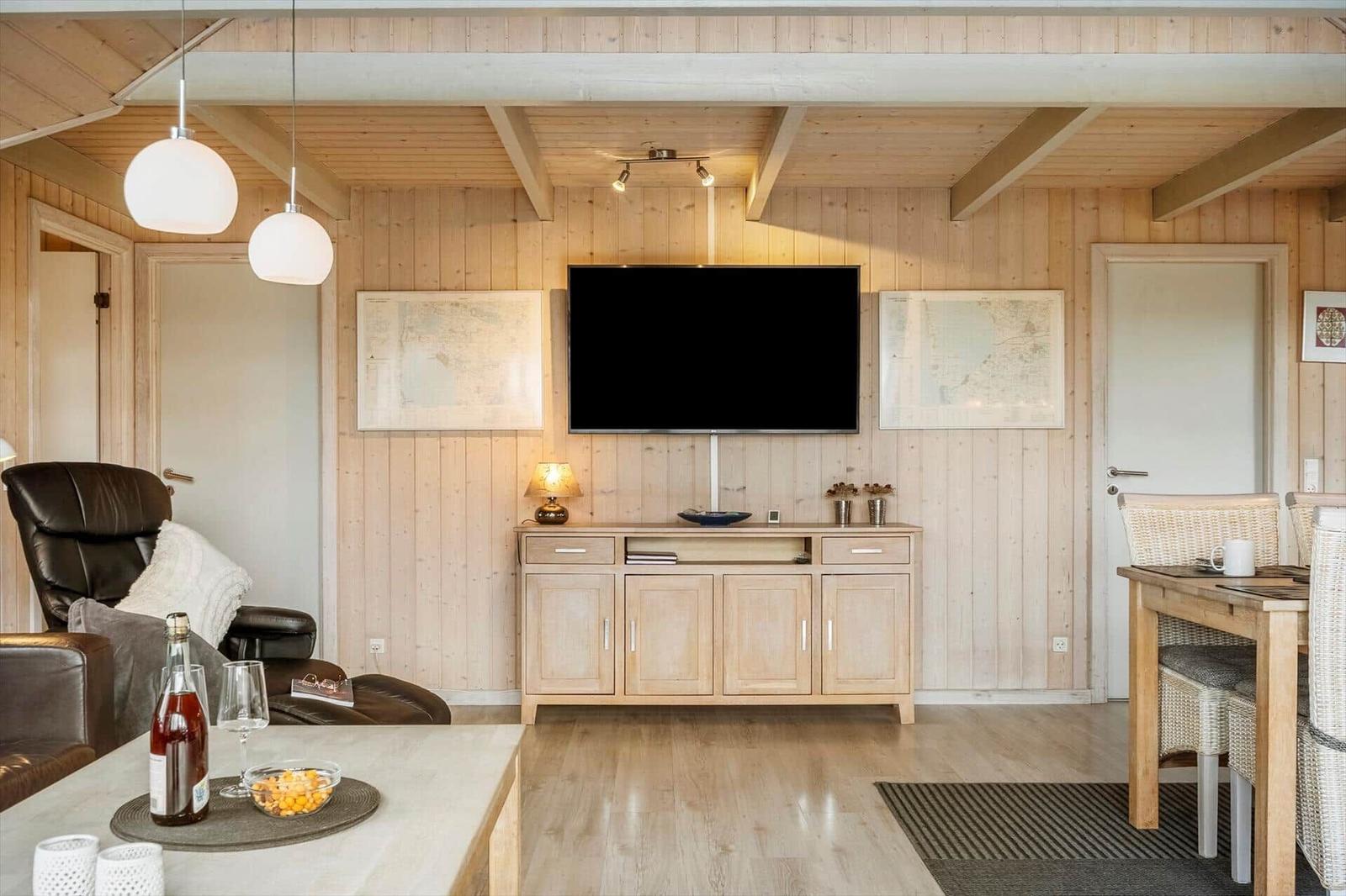 Wohnzimmer mit Fernseher, Holzwand und Essbereich.