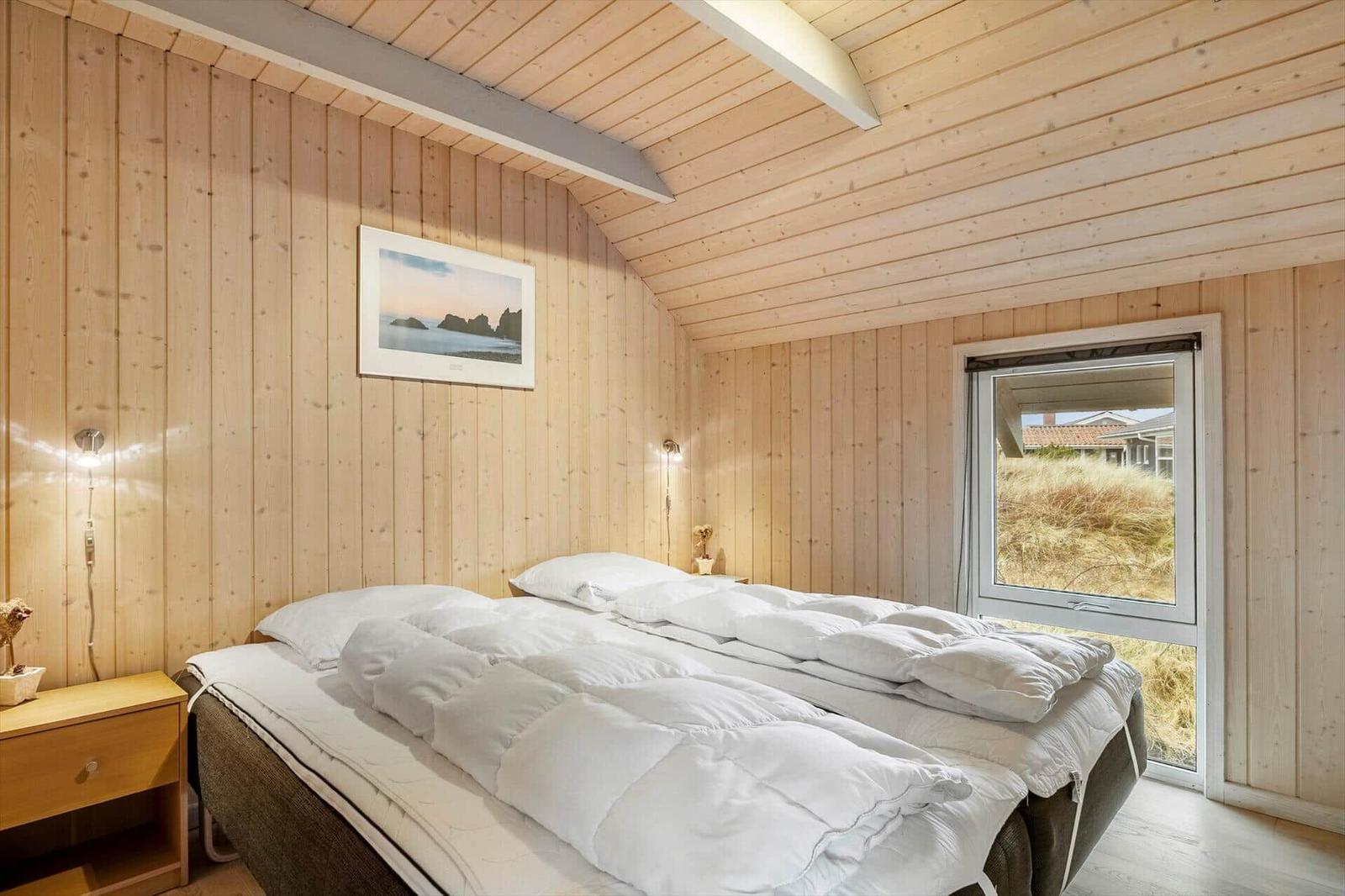 Schlafzimmer mit Holzwand, Bett und Fensterblick.