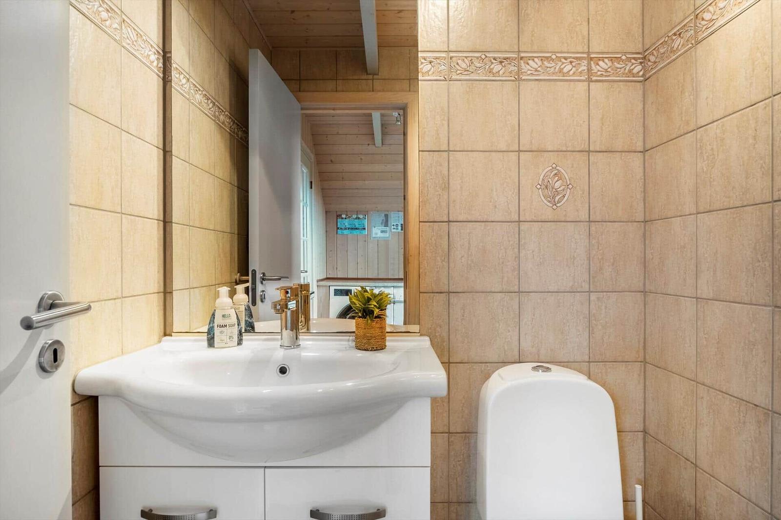 Badezimmer mit Waschbecken, Spiegel und Toilette. Fliesenwand mit dekorativer Bordüre.