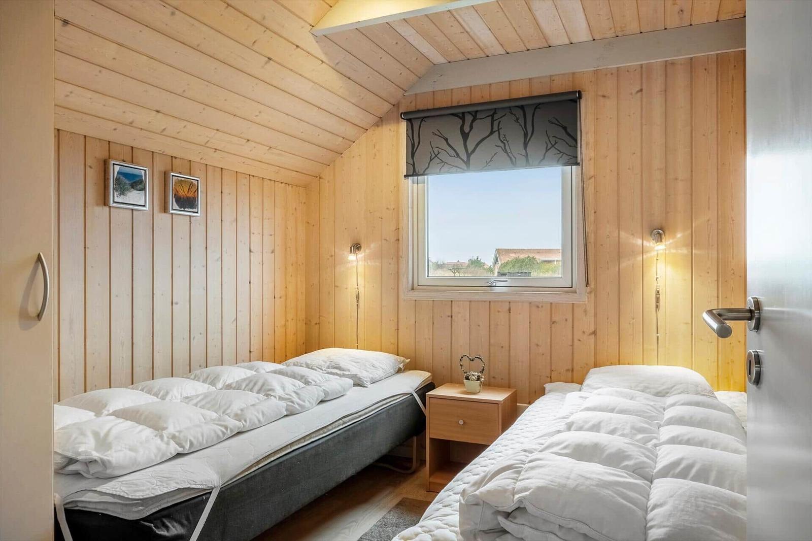 Zwei Betten in einem Holzhauszimmer mit Fenster und Nachttisch.