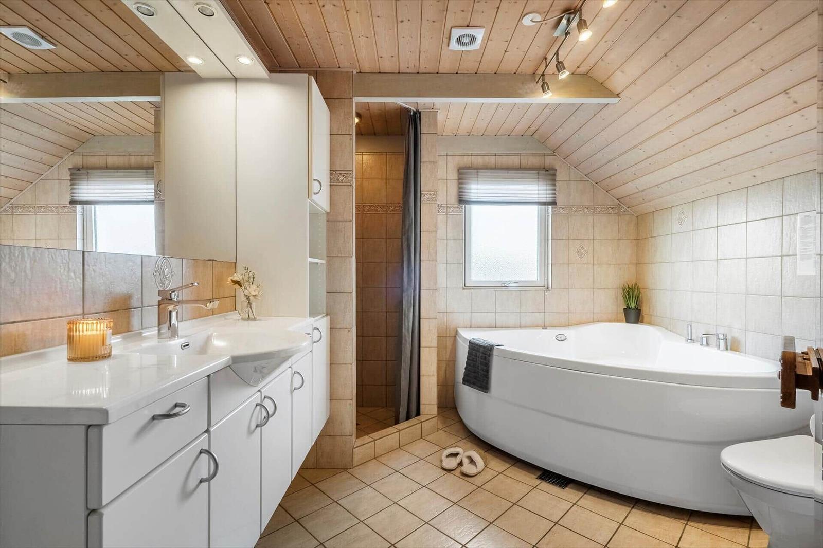 Badezimmer mit Badewanne, Dusche und Waschbecken unter Holzdecke.