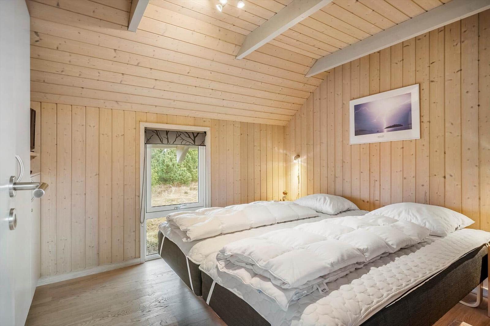 Schlafzimmer mit Holzwand und Bett. Fenster zeigt Außenbereich.