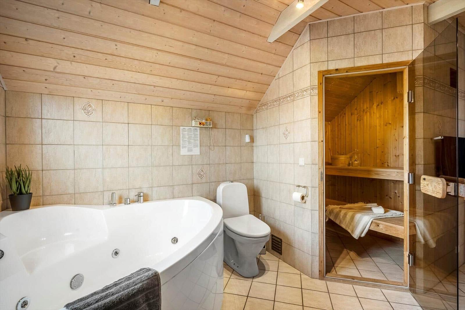 Bad mit Whirlpool, Toilette und Sauna im Hintergrund.