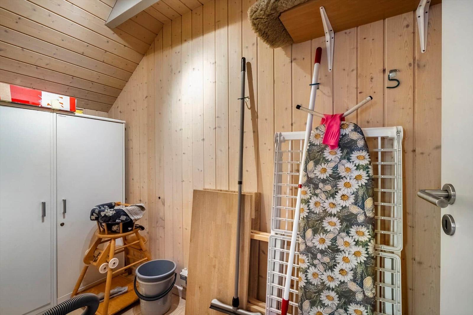 Raum mit Holzwänden, Kleiderständer, Staubsauger und Kinderstuhl.