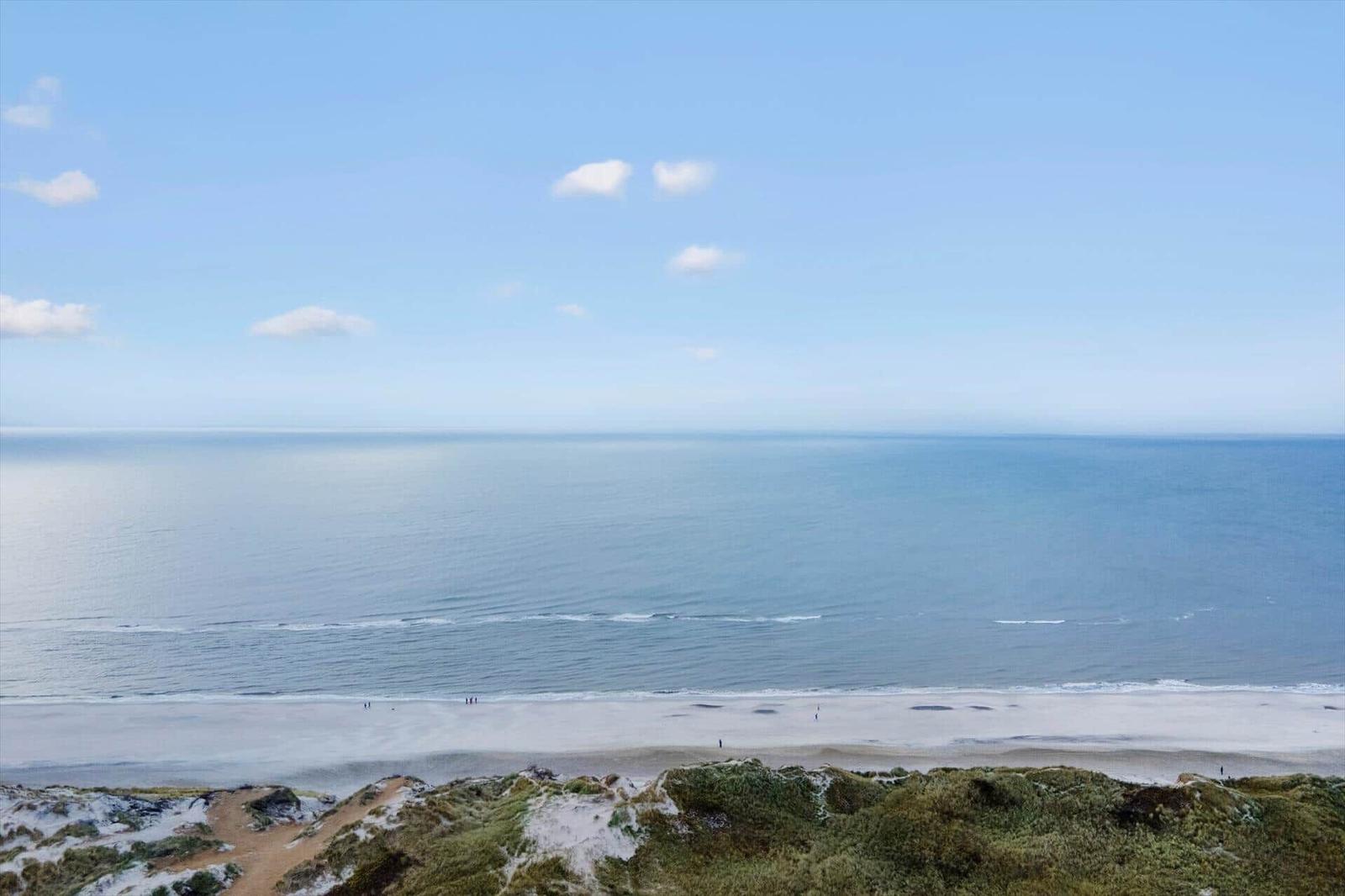 Weitläufiger Strand mit sanften Wellen unter klarem Himmel.