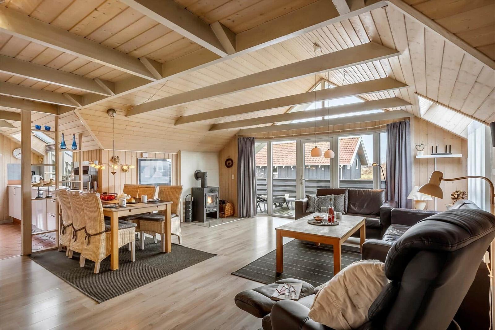 Wohn- und Essbereich mit Holzdecke, Sofa, Esstisch und Blick auf die Terrasse.