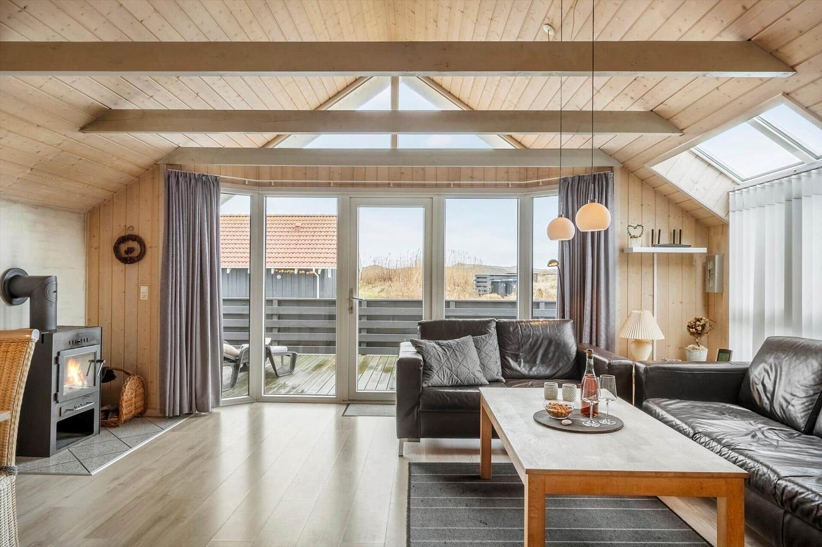 Wohnzimmer mit Holzdecke, Sofa, Kamin und Blick auf Terrasse.